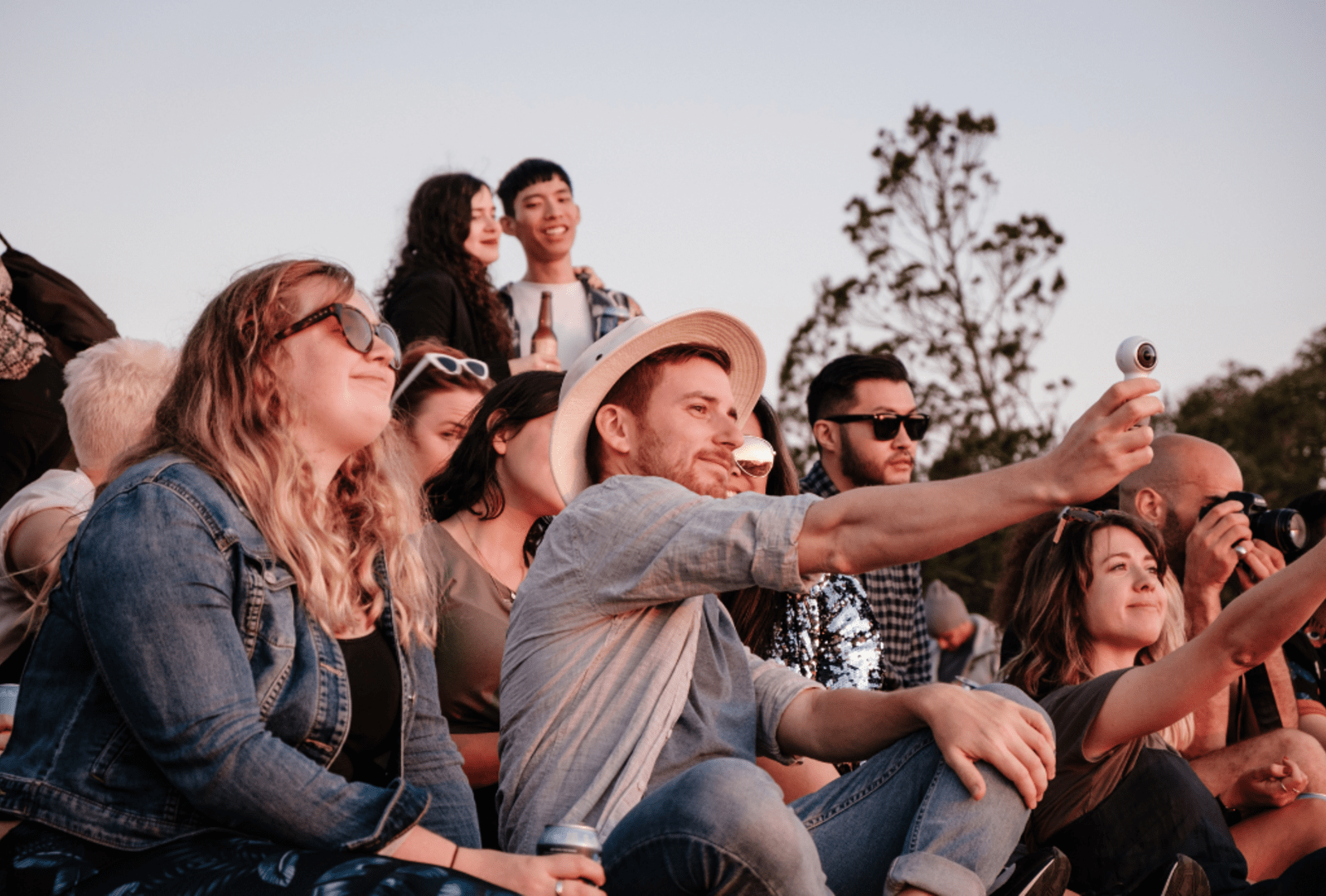 Young people sit on a hill watching an outdoor event.