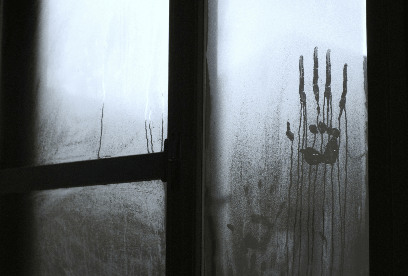 A ghostly handprint drips down a foggy window