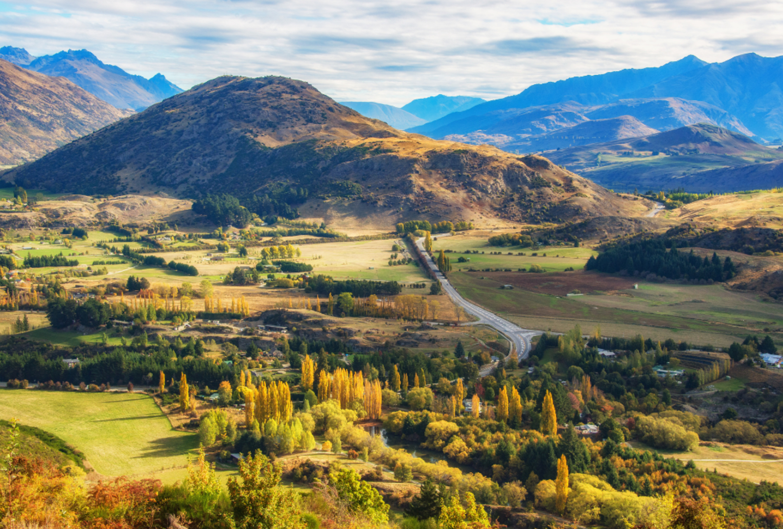 A road runs through green rolling hills with mountains in the background