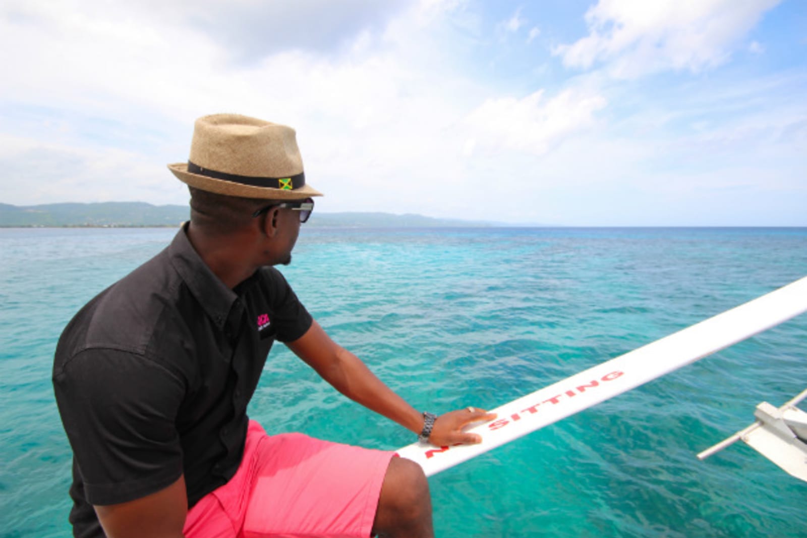 Man with a hate staring out at the water from the edge of his catamaran