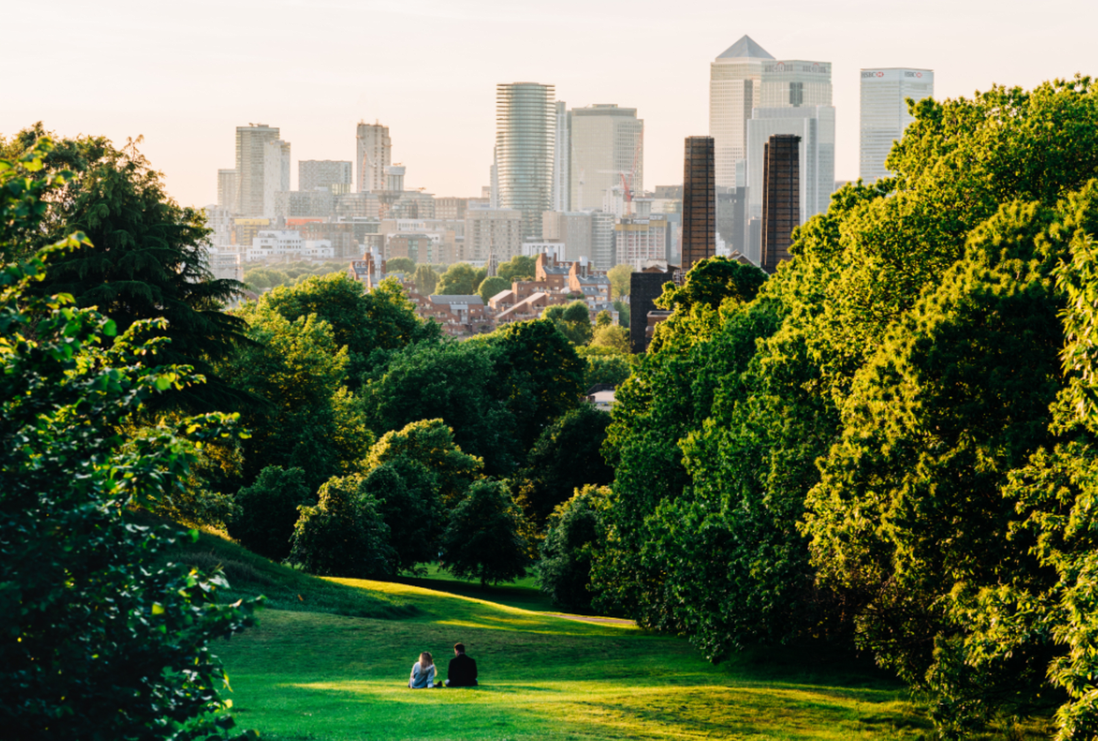 A couple sit in Greenwich Park, London looking the Canary Wharf 
