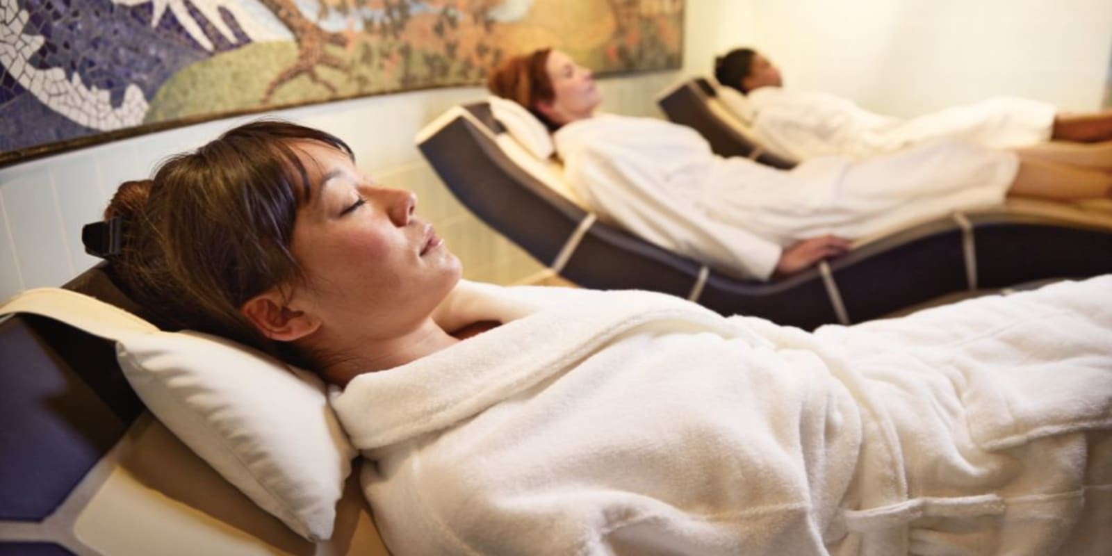 Three women wearing robes and laying on bed in a spa and massage parlour