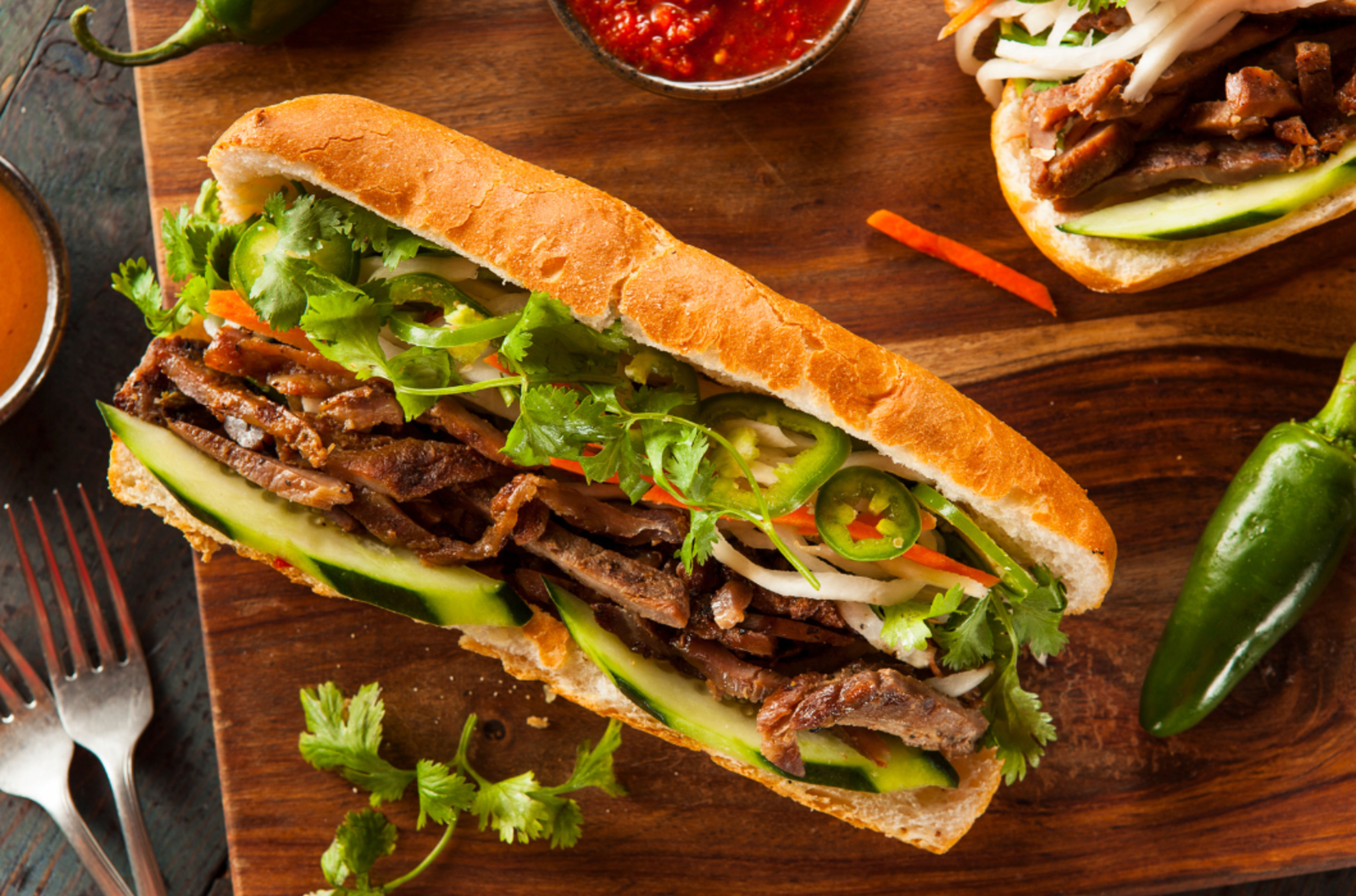 Vietnamese banh mi baguette sitting partially open on a wooden chopping board.