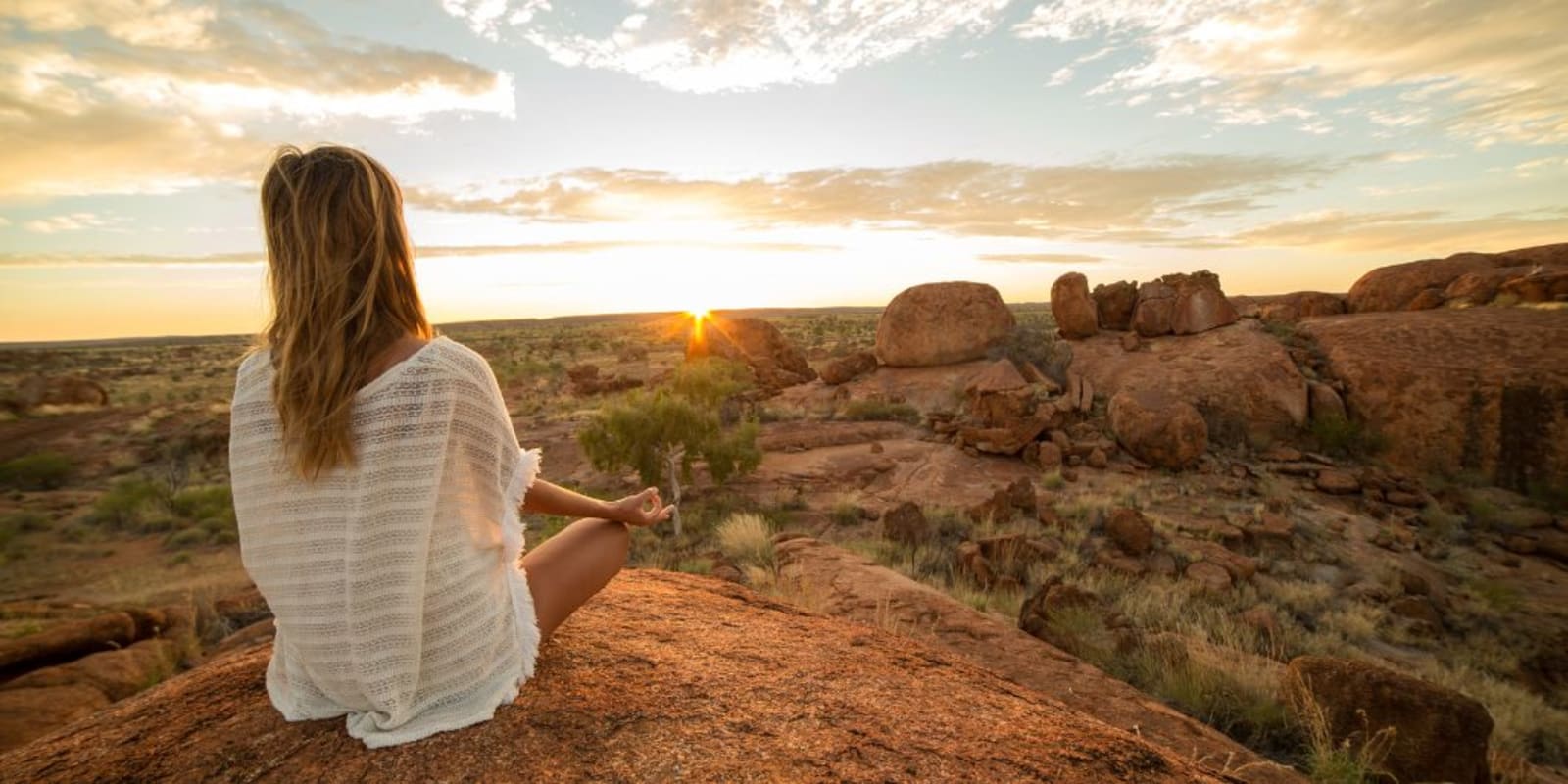 A relaxed person sitting on the ground meditating as the sun rises