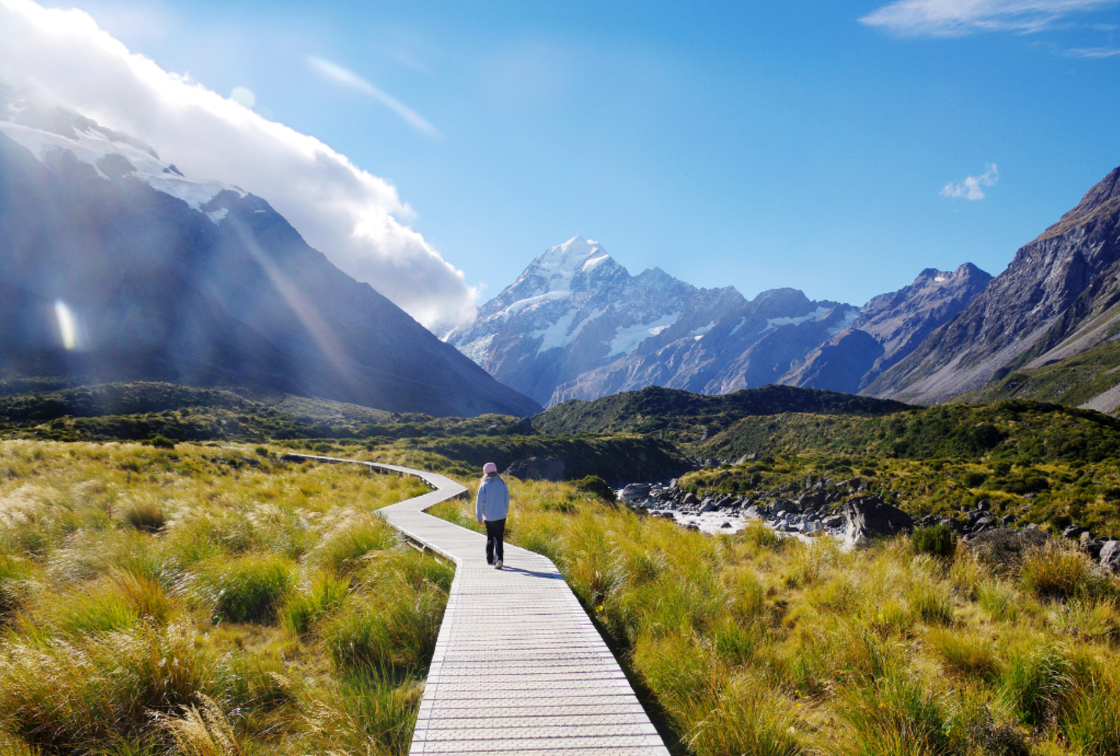 Girl walking on boardwalk at Hooker Valley Track, with view of Mount Cook.