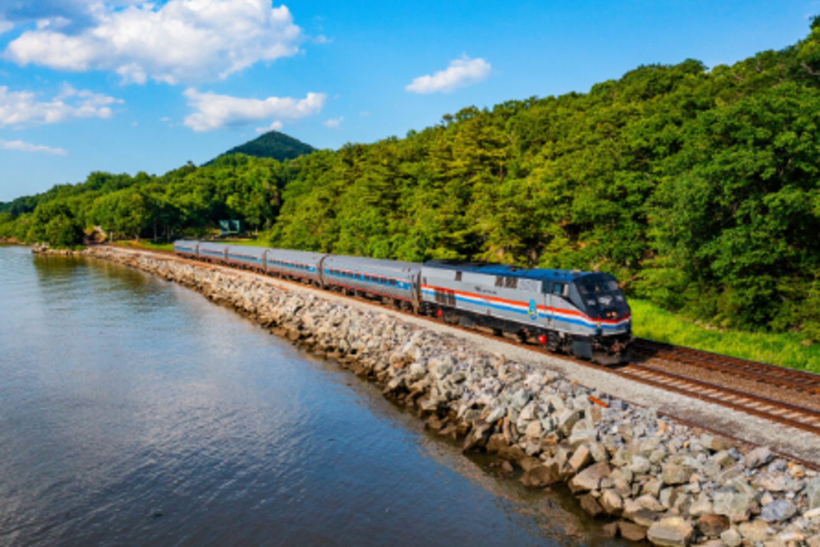 amtrak train running along train line with water on one side and trees on the other