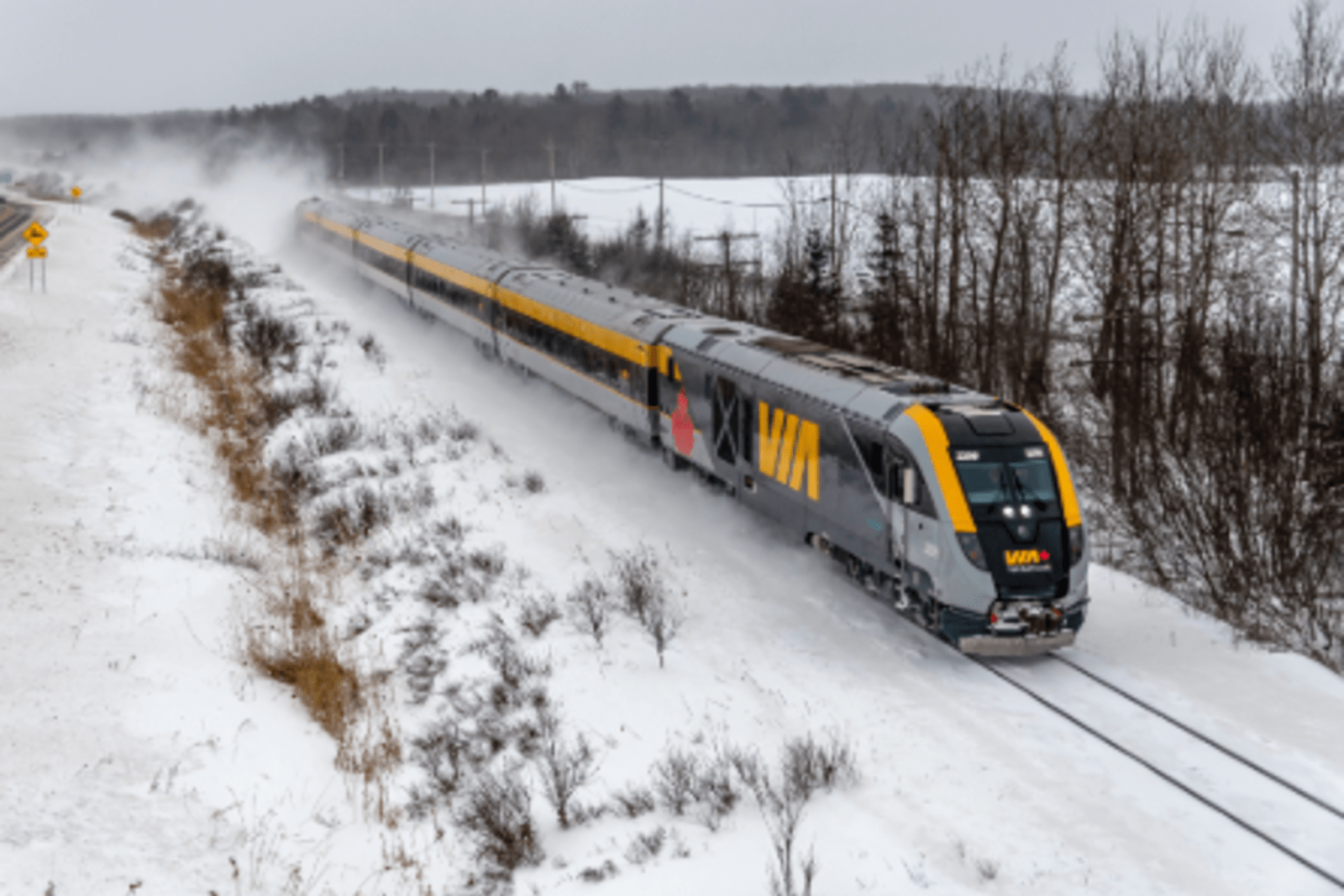 via rail canada train travelling along icy track with trees and mountains in background
