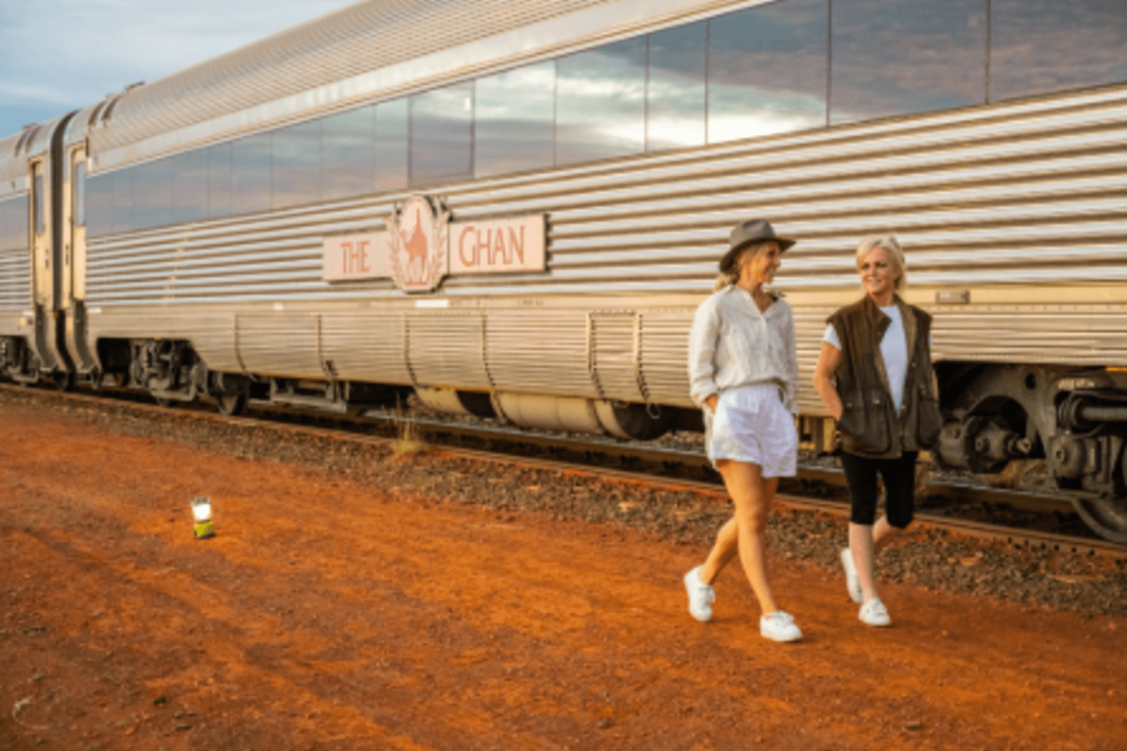 two ladies walking beside the ghan train with red desert underneath