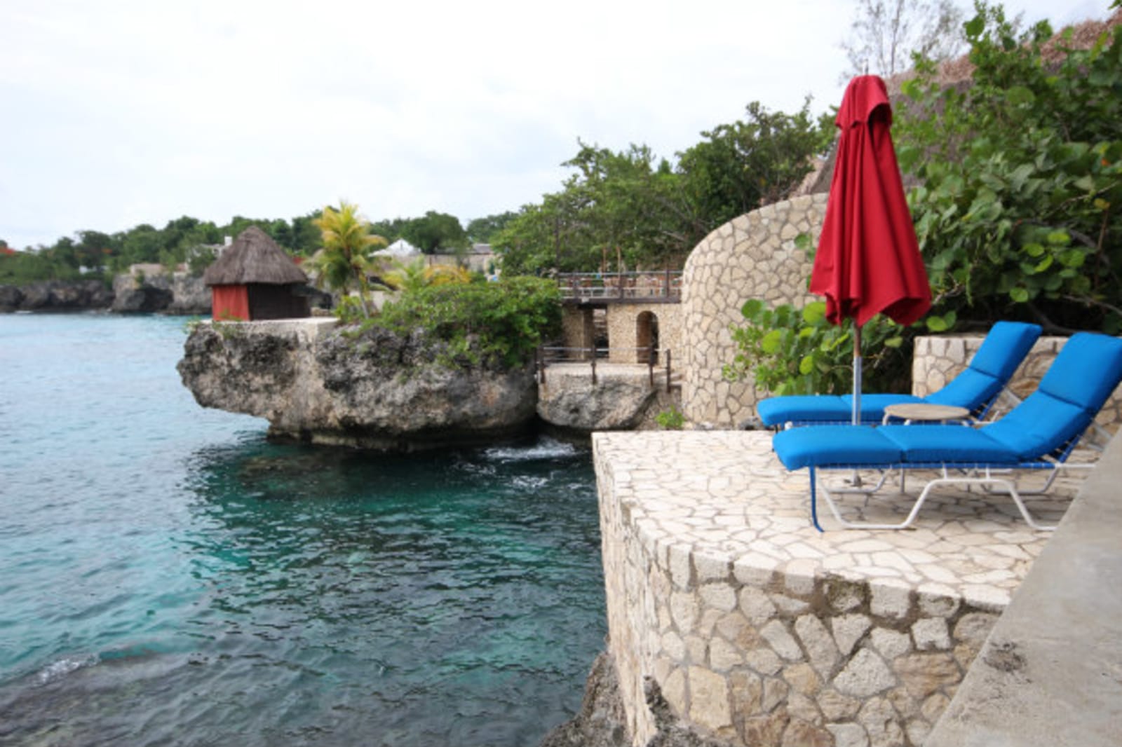 Two blue deck chairs under a red umbrella on a smooth rocky outlook
