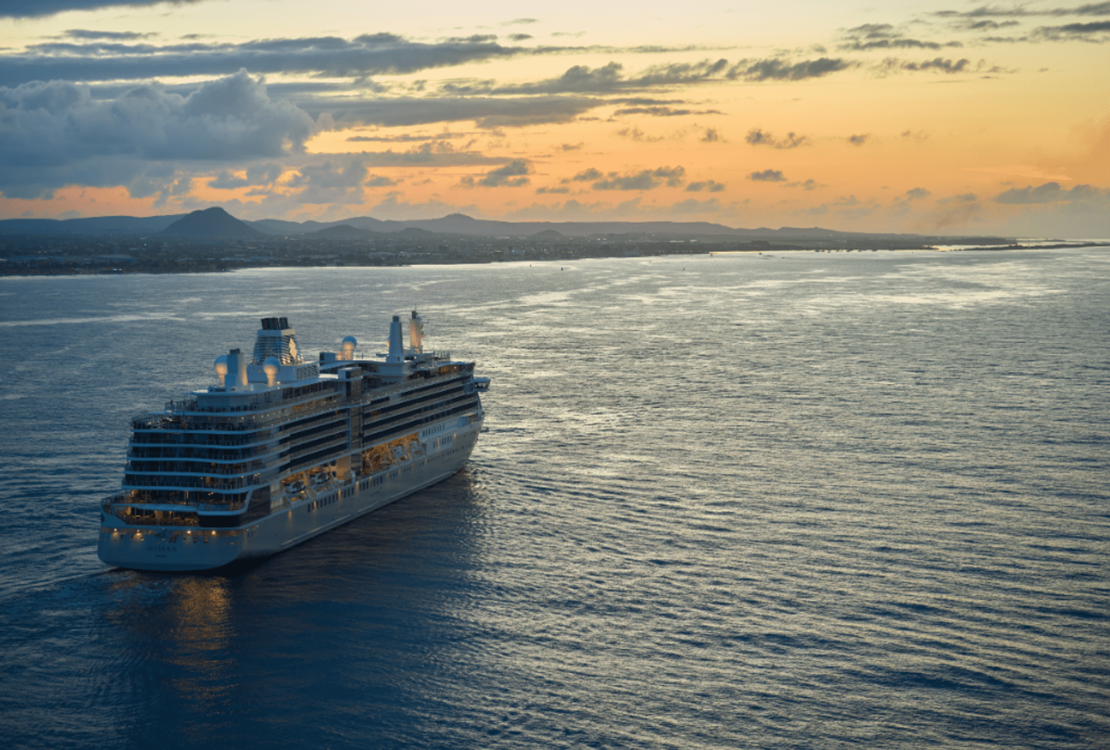 A luxury cruise ship sailing away from the coast as the sun sets