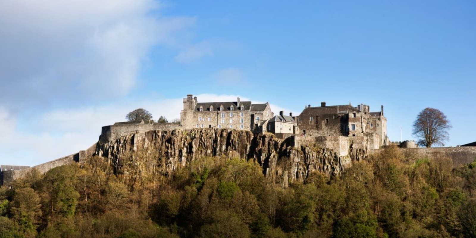 Stirling Castle sitting on top of a steep cliff with trees at the base