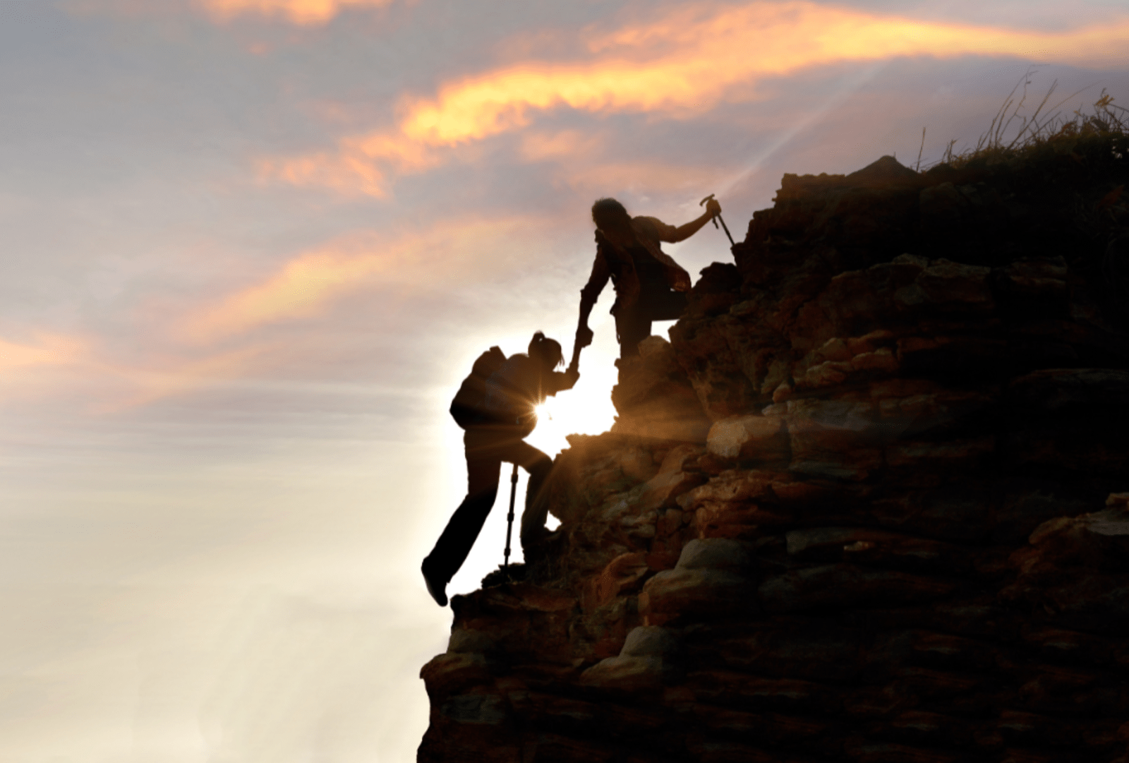 Two silhouetted hikers scaling a cliff