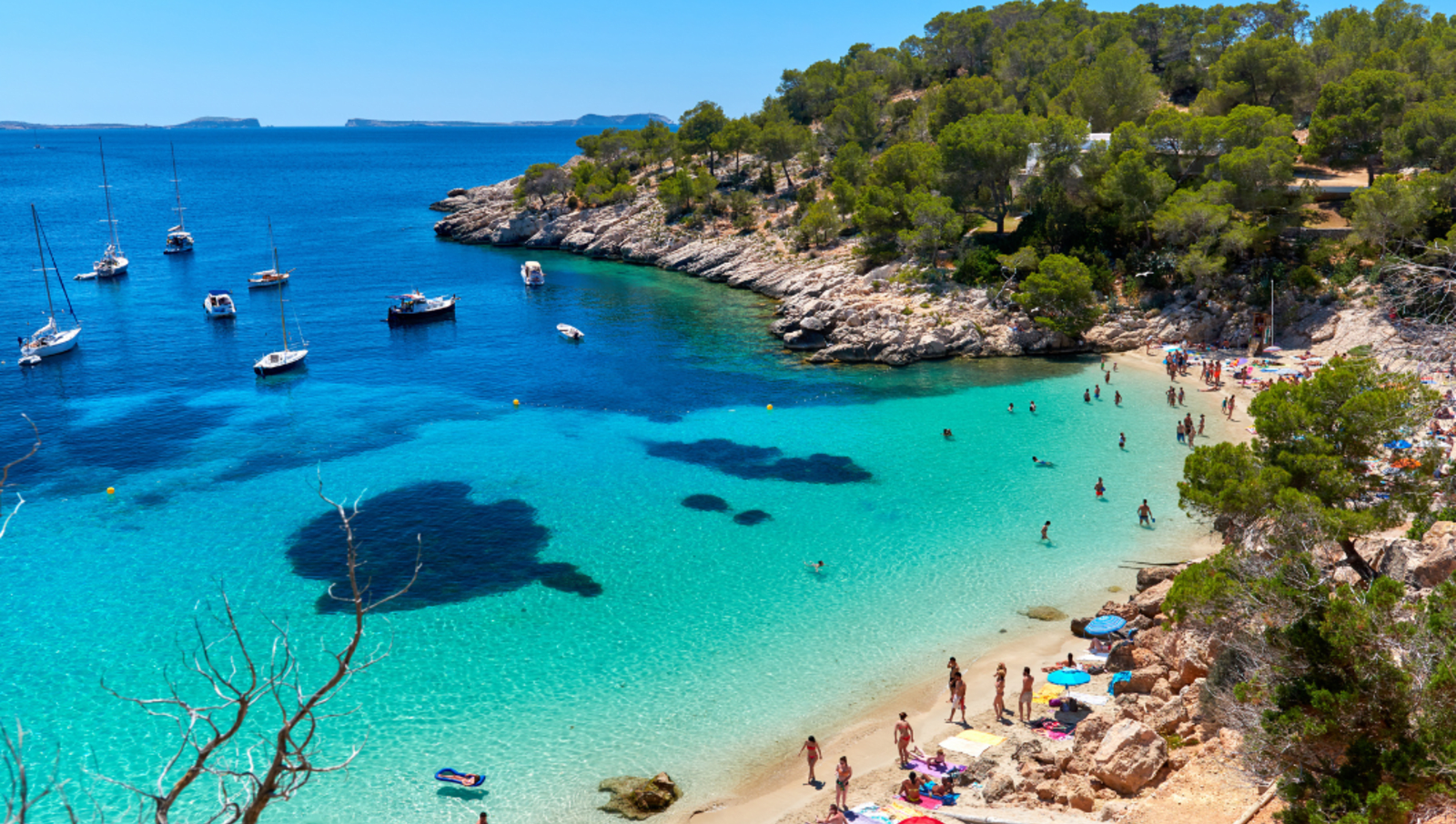 beach on coast of ibiza with lots of people, boats and umbrellas