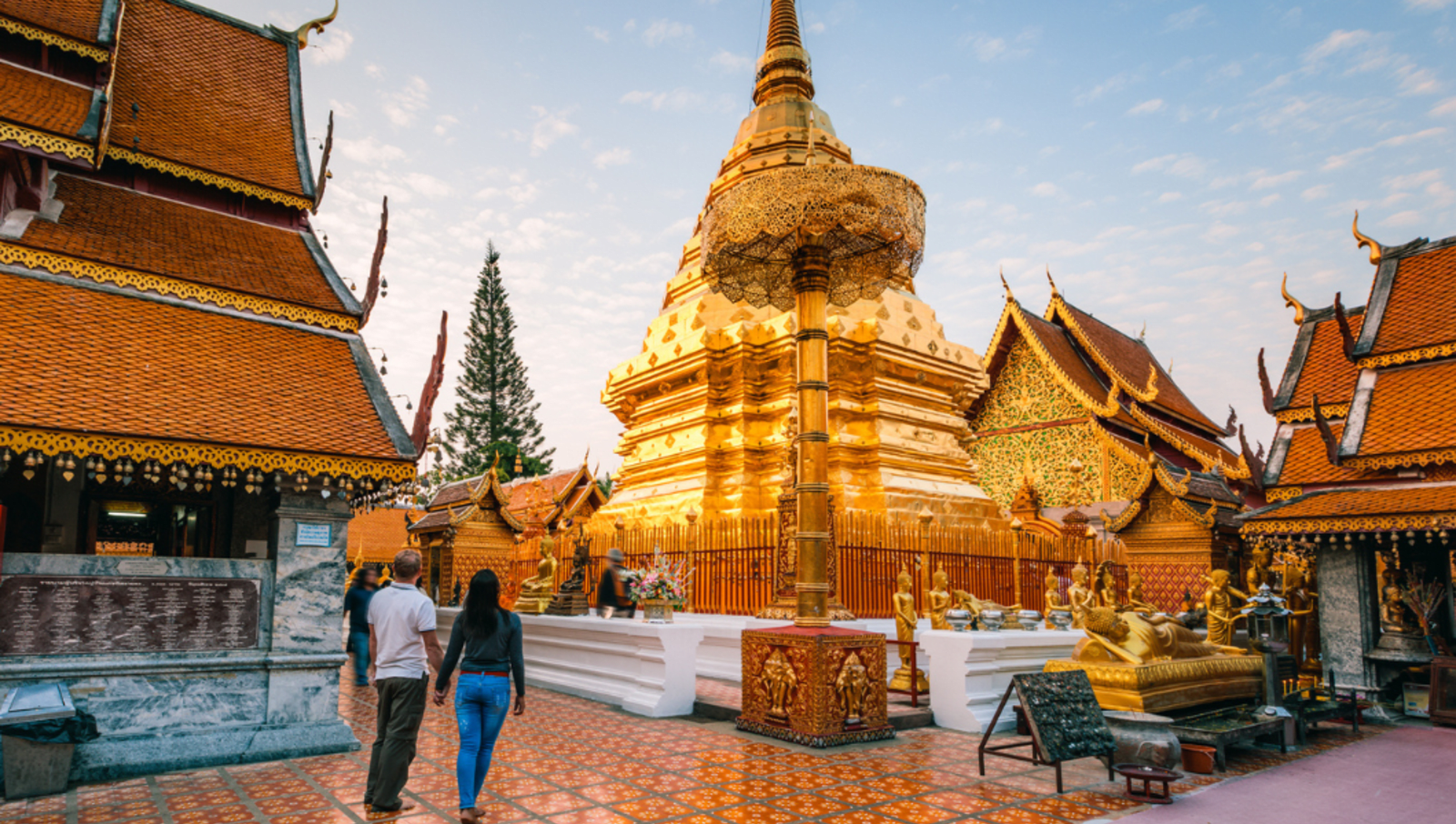 Couple holding hands while looking at large gold temple in Thailand