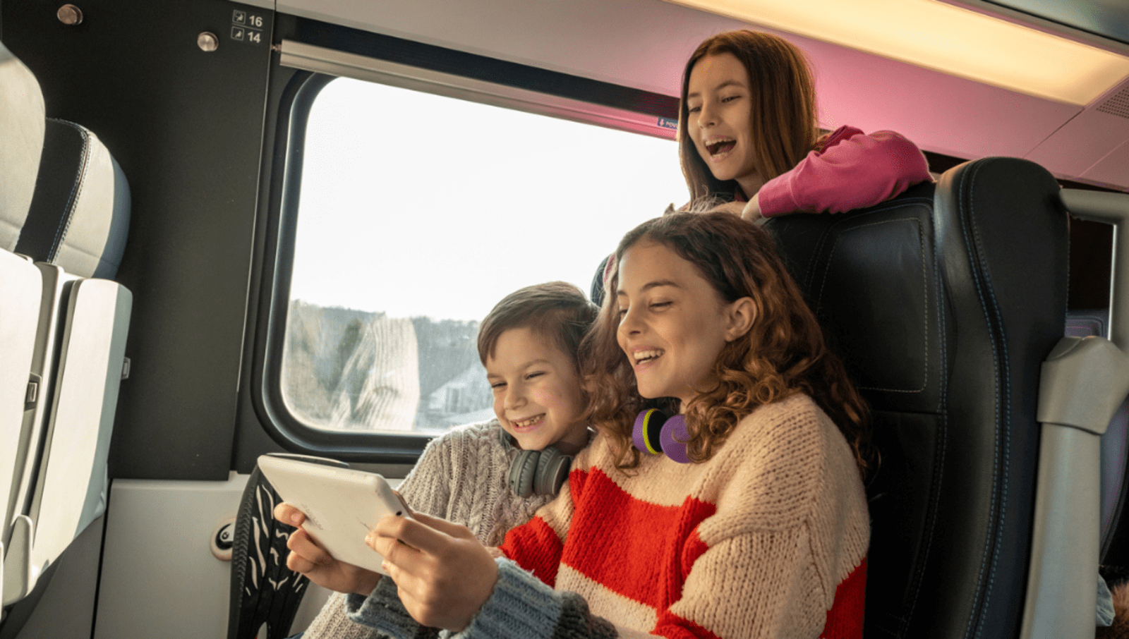 Three children on a train looking at one tablet with their headphones 