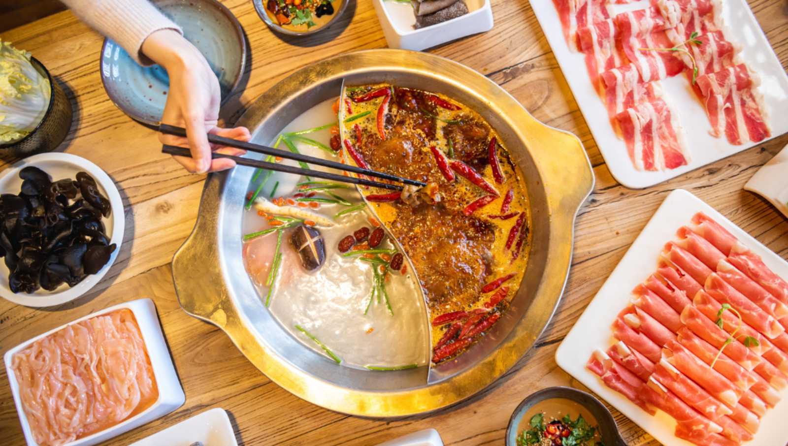 hand using chopsticks to cook meat in pot of hot soup