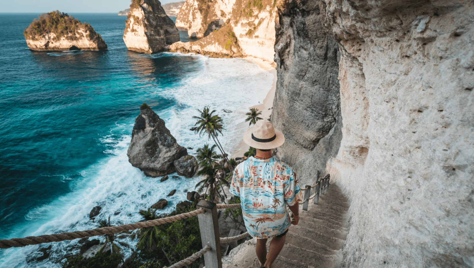 man walking down stairs on cliffside towards beach