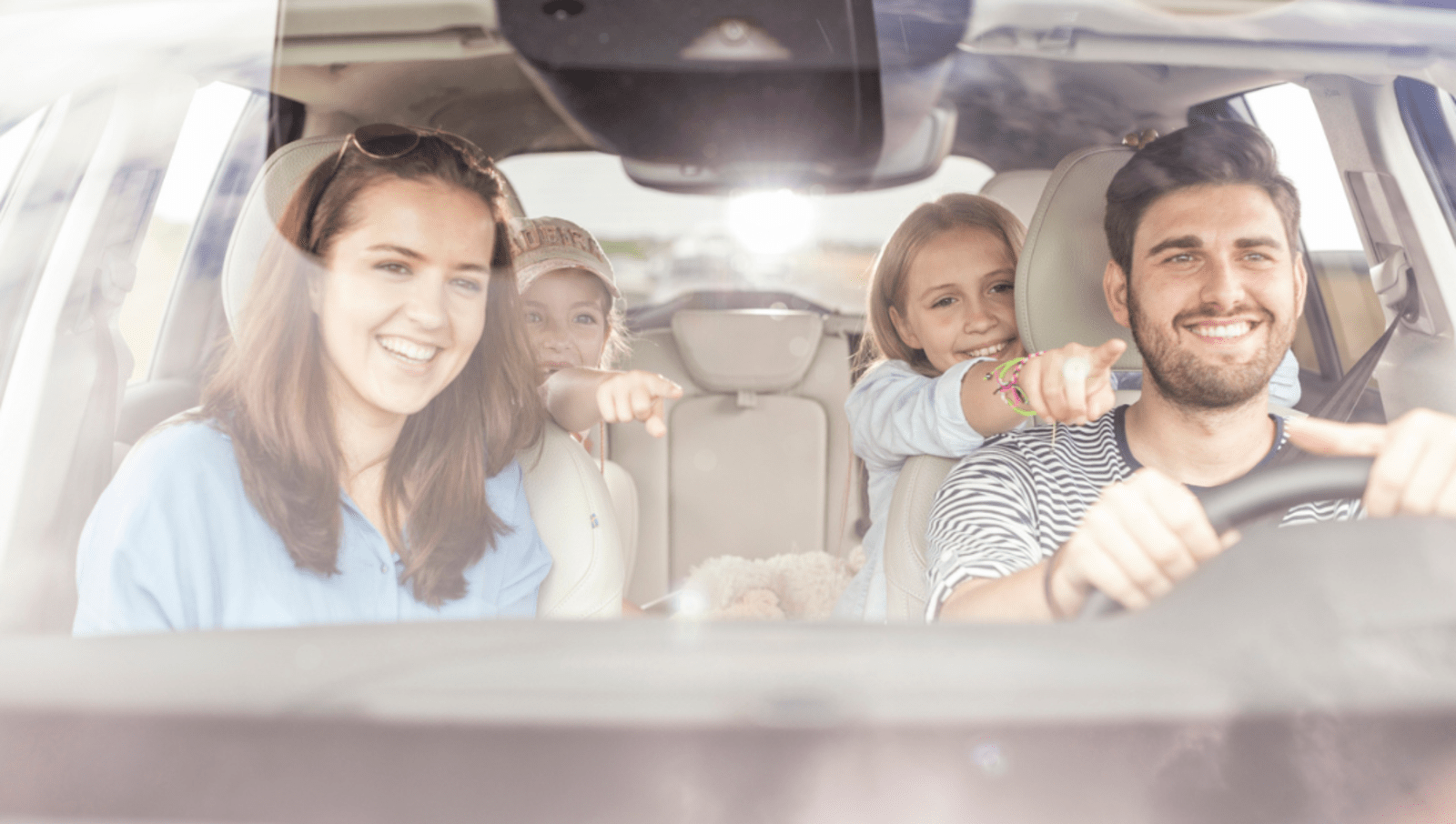 Dad, mother and two daughters sitting in a car while they all smile and the girls point 