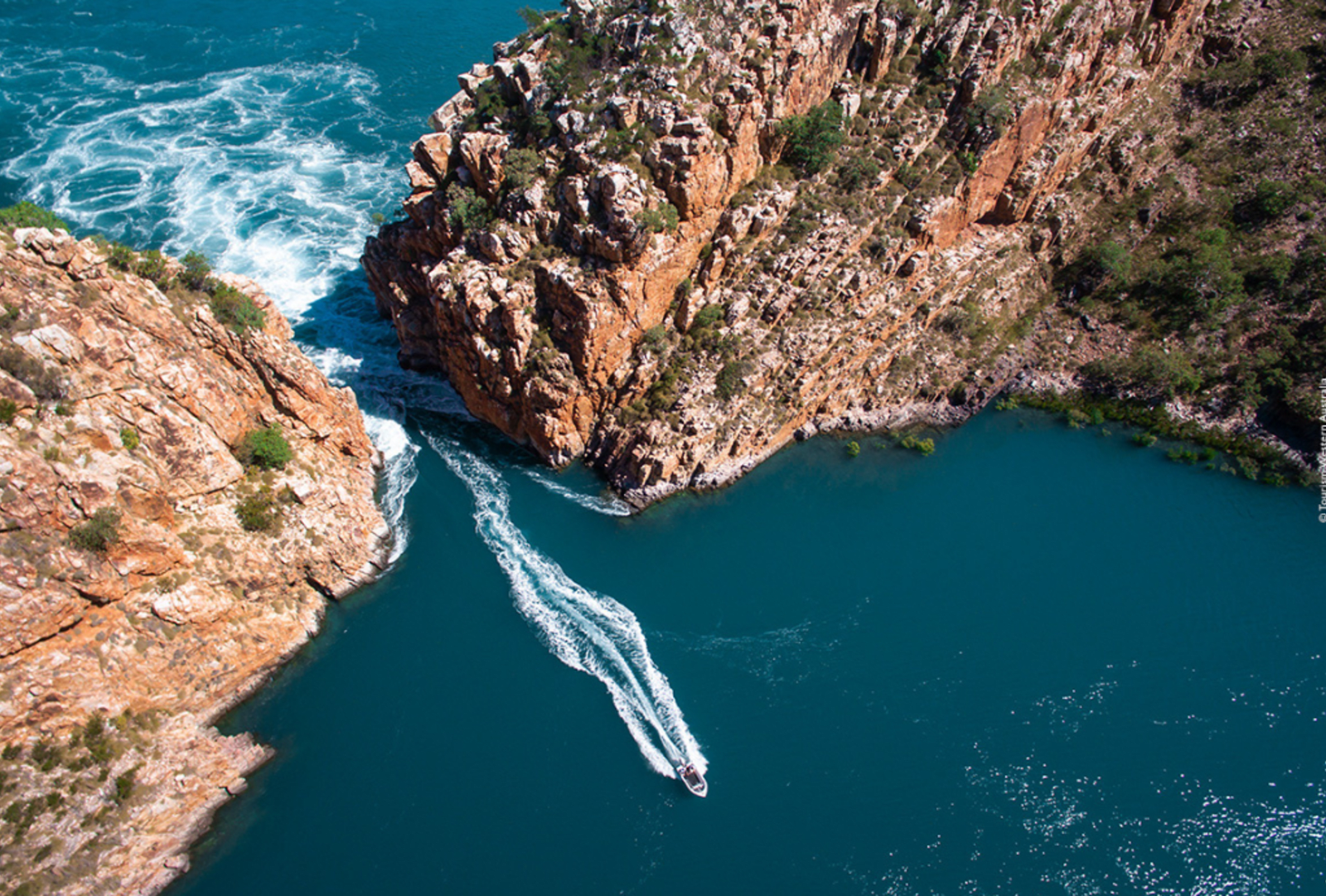A drone's view of a jet boat heading away from sea rapids between to rocky peninsulas