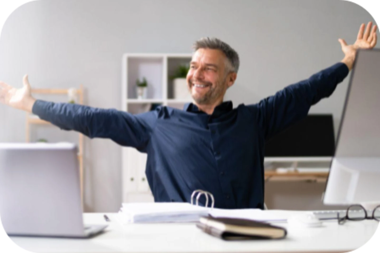 a man sits in office with a big smile and arms wide open 
