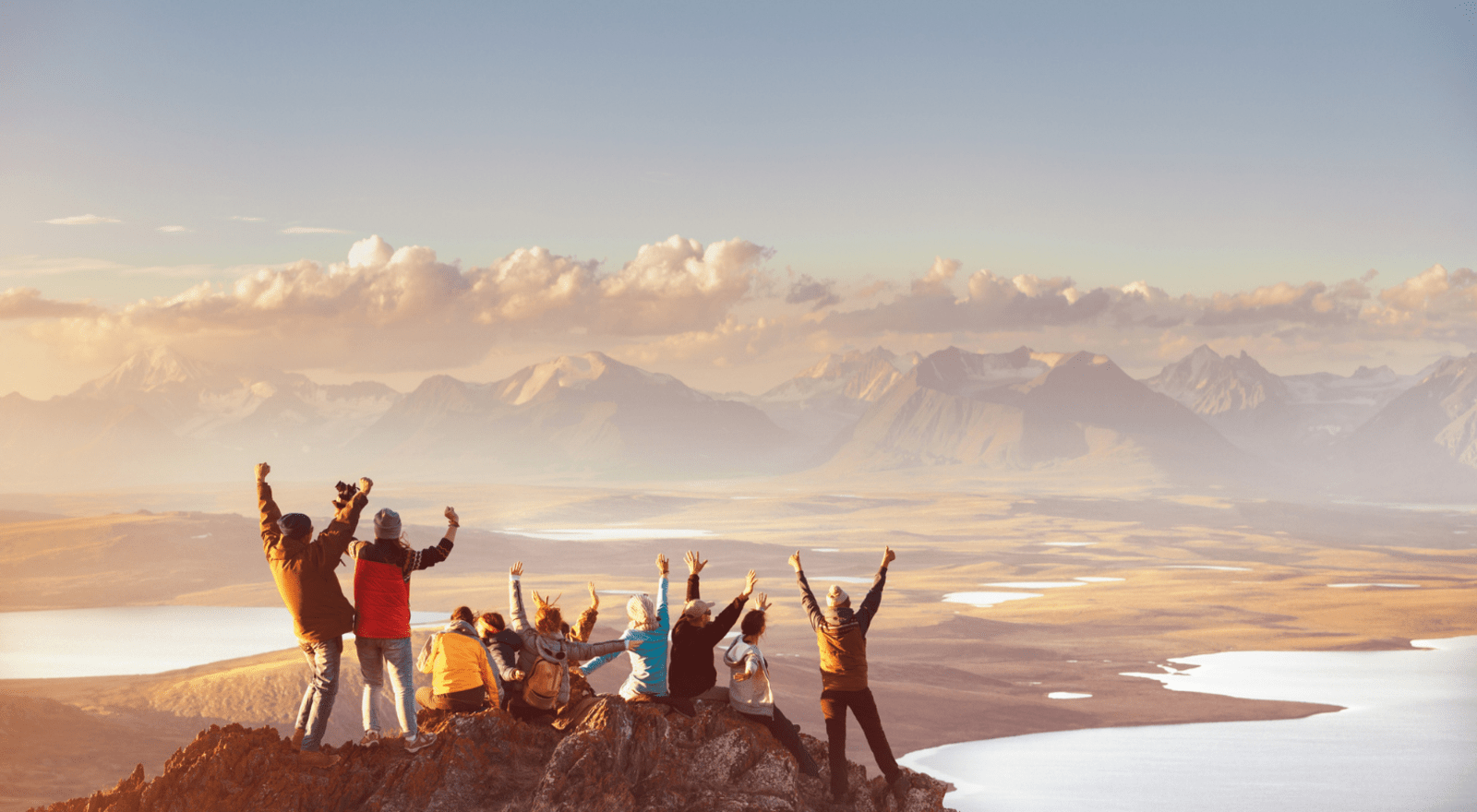 group of friends on mountain top with arms up