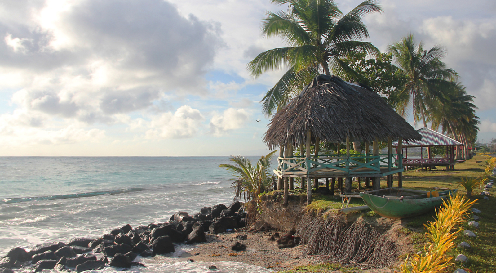 rocky coastline with palm trees and small huts at sunset