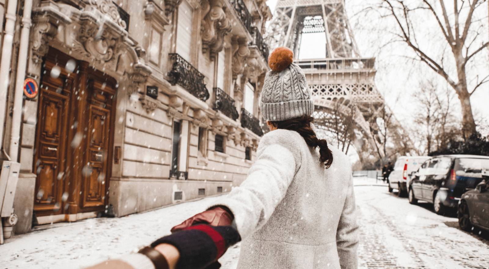 Lady wearing beanie walking in front of camera in snow near eiffel tower