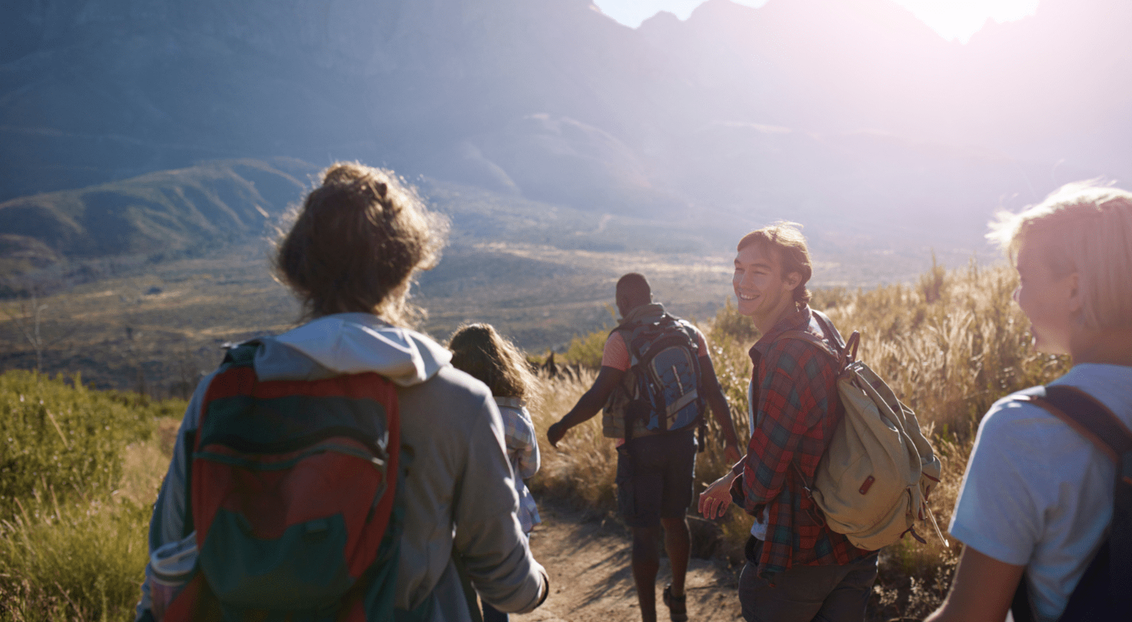 group of young people with backpacks walking through hilly and grassy area 