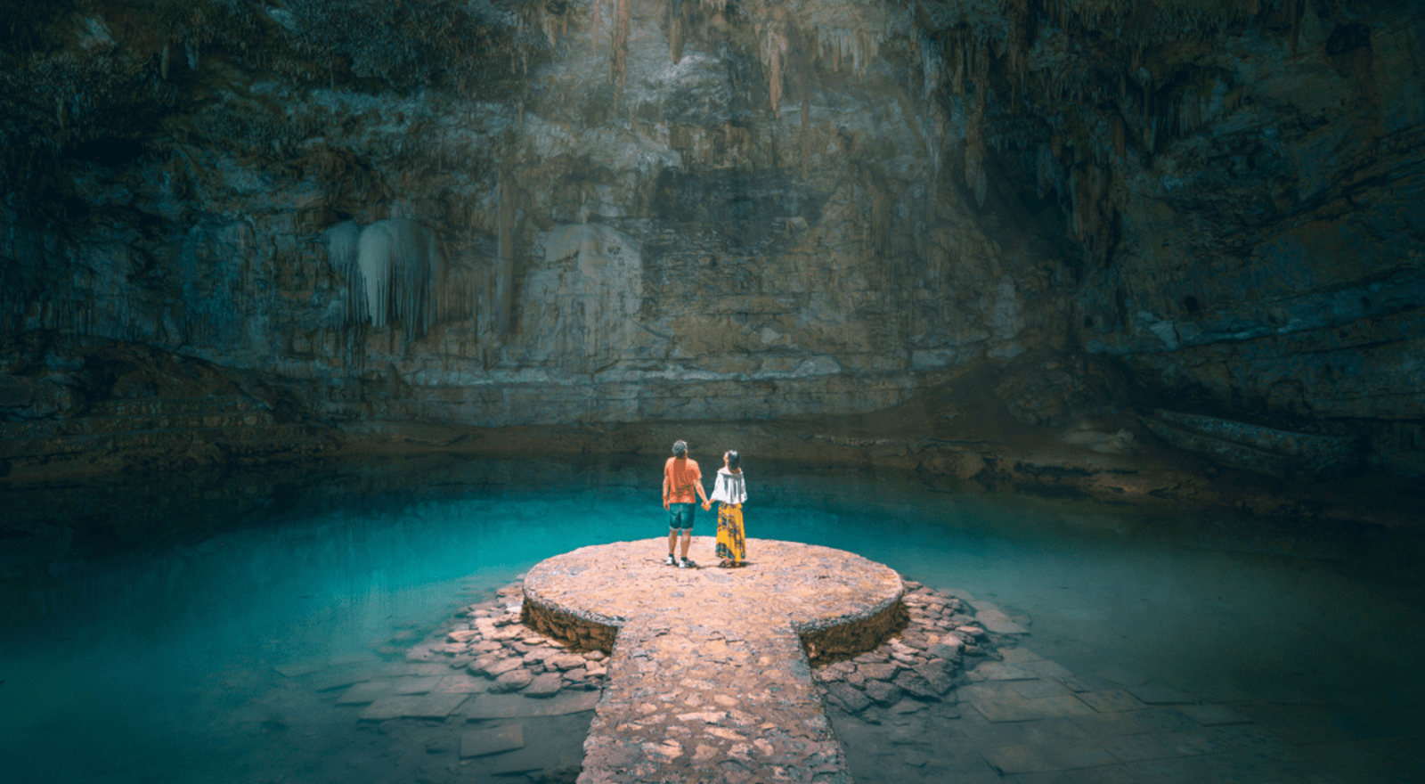 couple holding hands standing in a cave on a platform surrounded by water