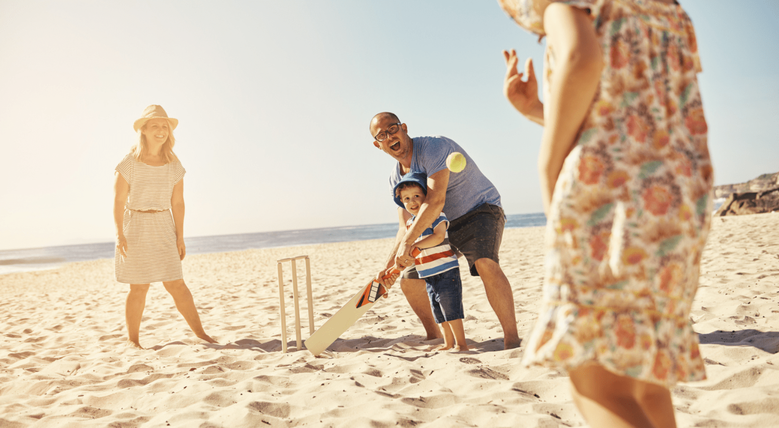 family of four playing cricket on beach