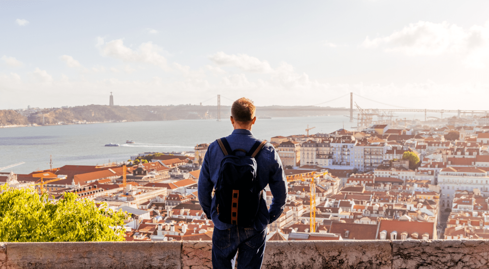 Man with backpack looking out at Lisbon city and river