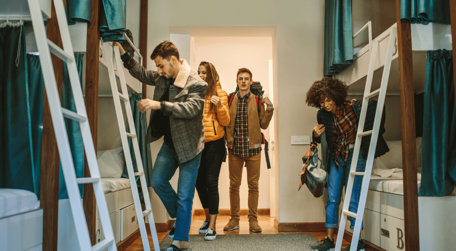 Four young people with backpacks entering room in hostel