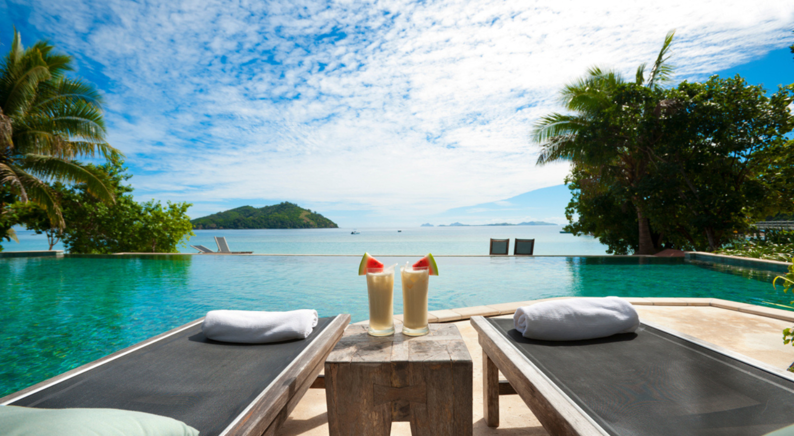 two chairs and two drinks on a table with pool and beach in the background