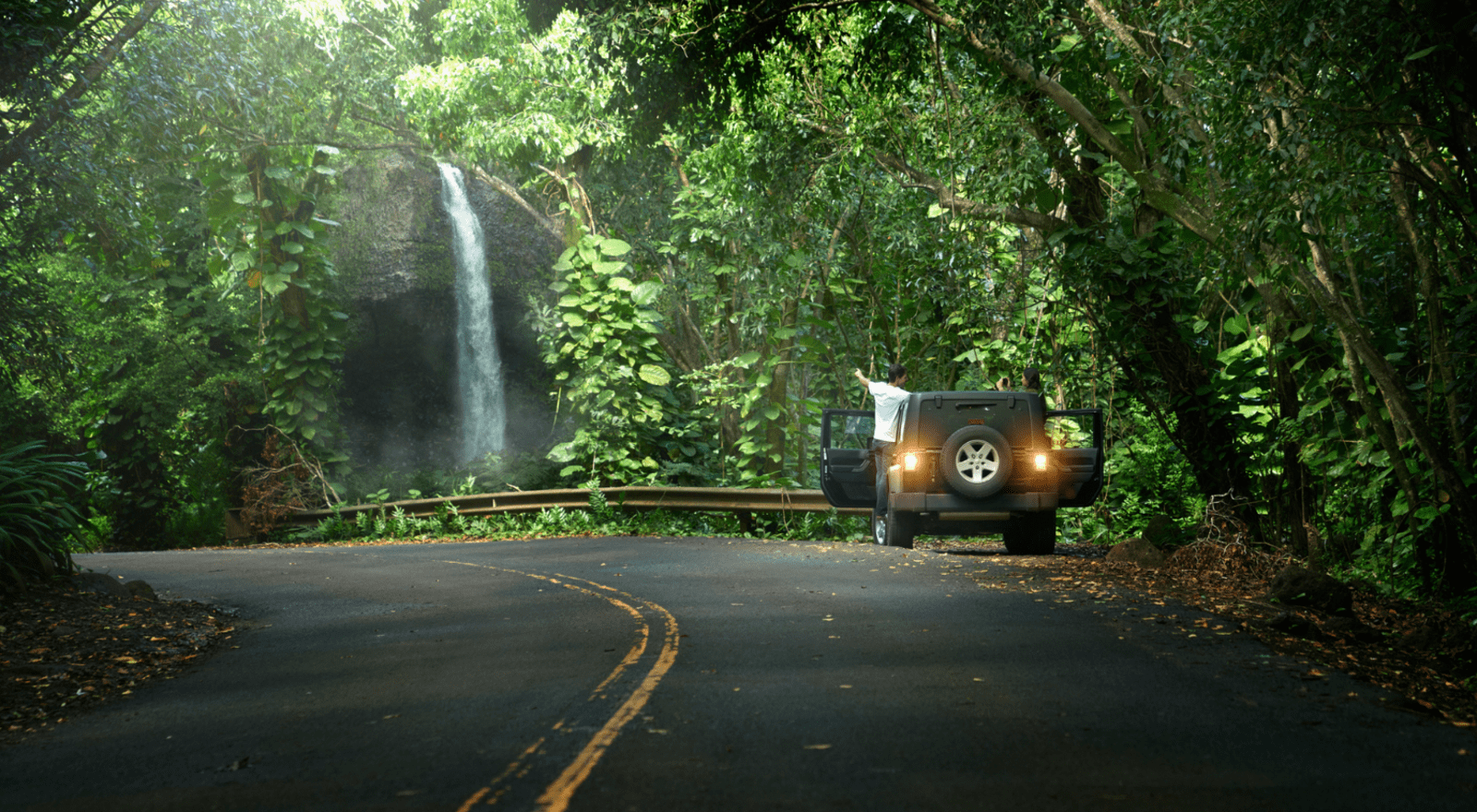 couple with car pulled over on side of road taking photos of waterfall