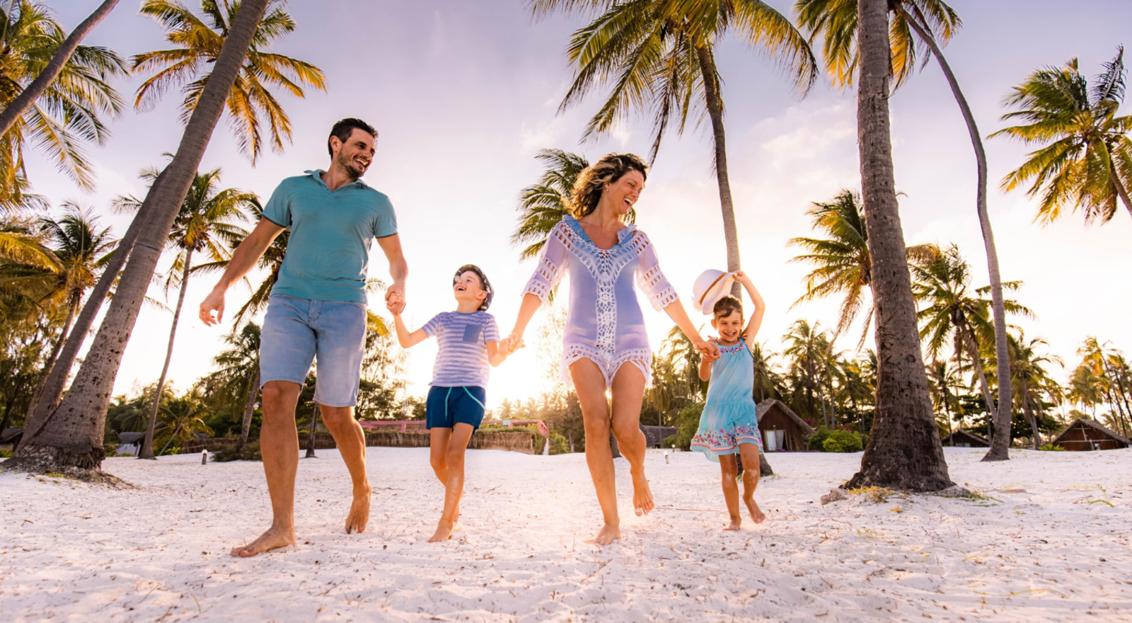 dad, mum, son and daughter holding hands and running on a beach in fiji with the sun behind them 