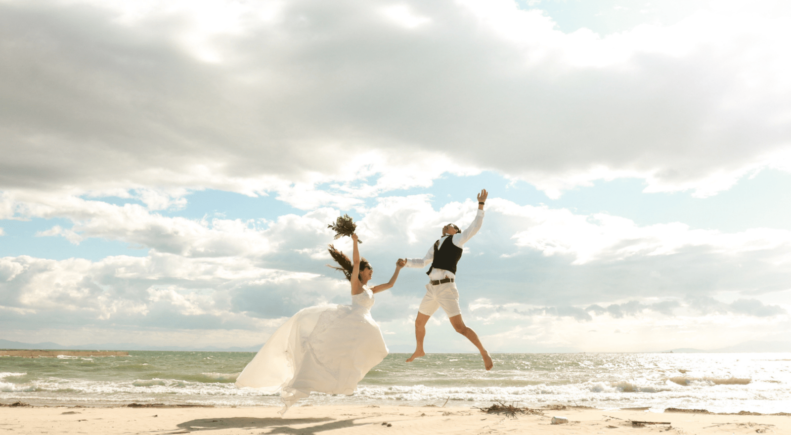 couple jumping in air on beach on their wedding day