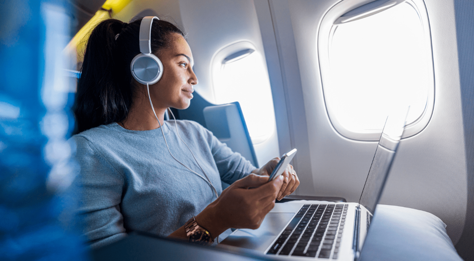 woman with headphones, laptop and phone looking out of an airplane window