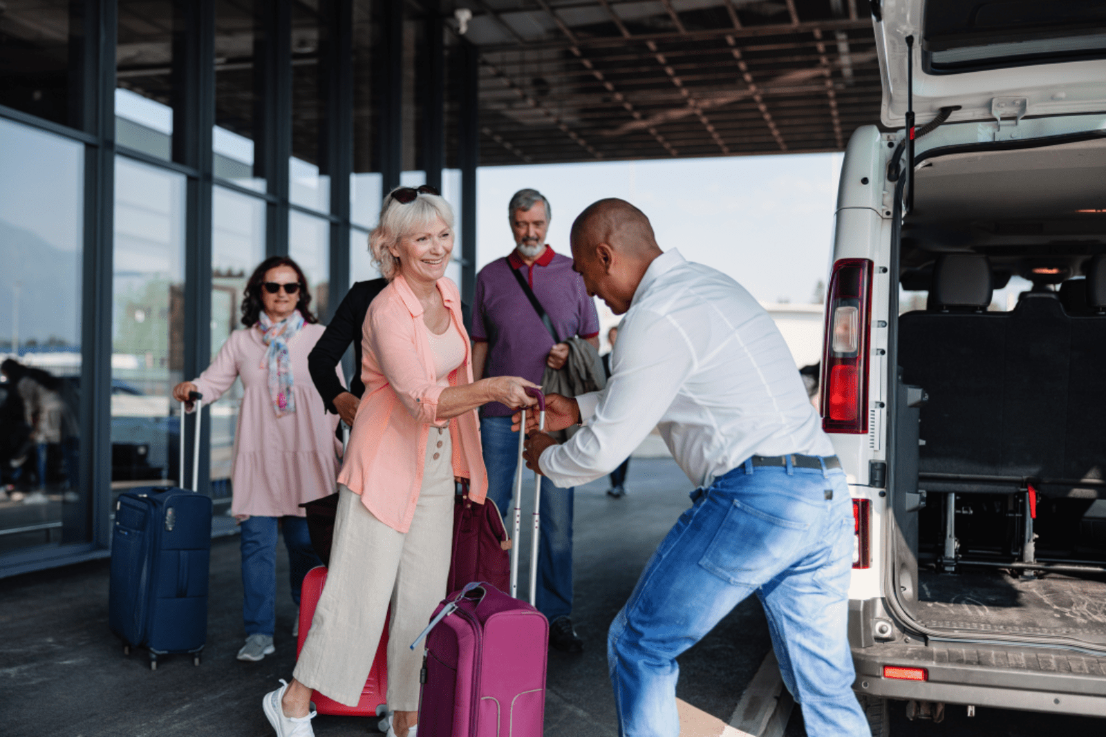 The driver of an airport transfer service helping passengers load their luggage into the shuttle