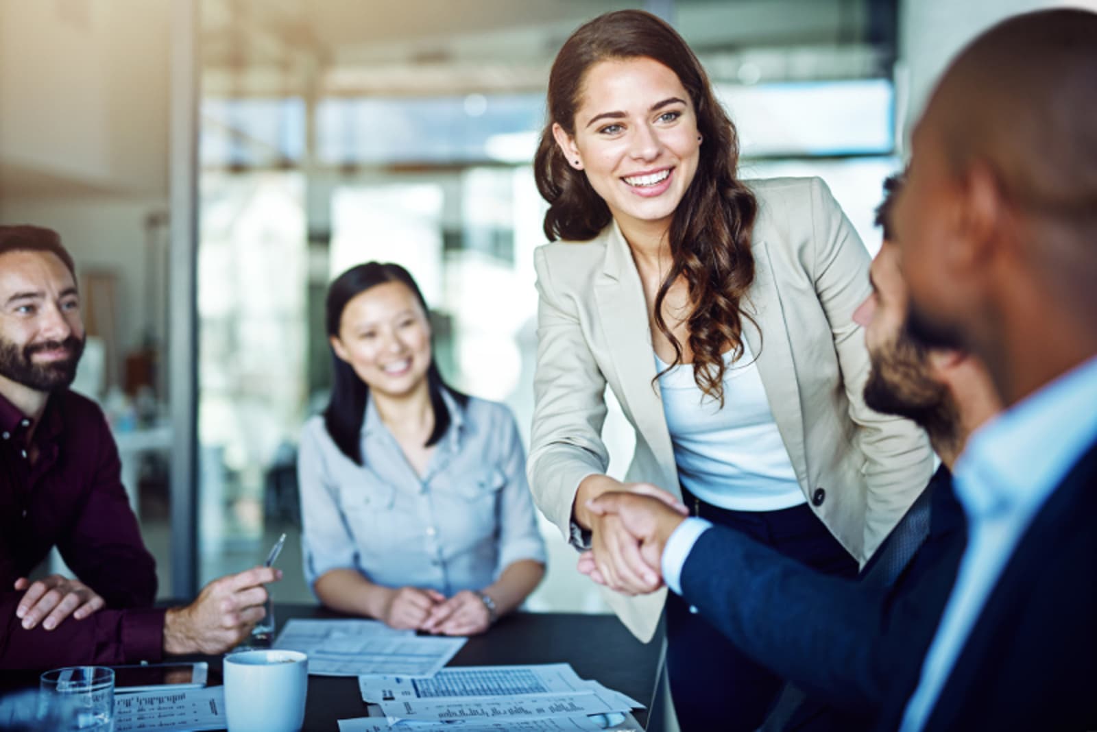 A young professional woman shaking hands with other professionals in a meeting
