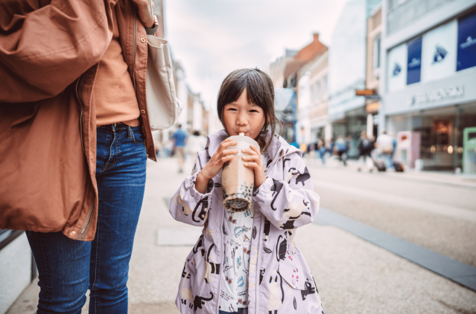Little girl wearing a purple jacket holding a large cup of bubble tea.