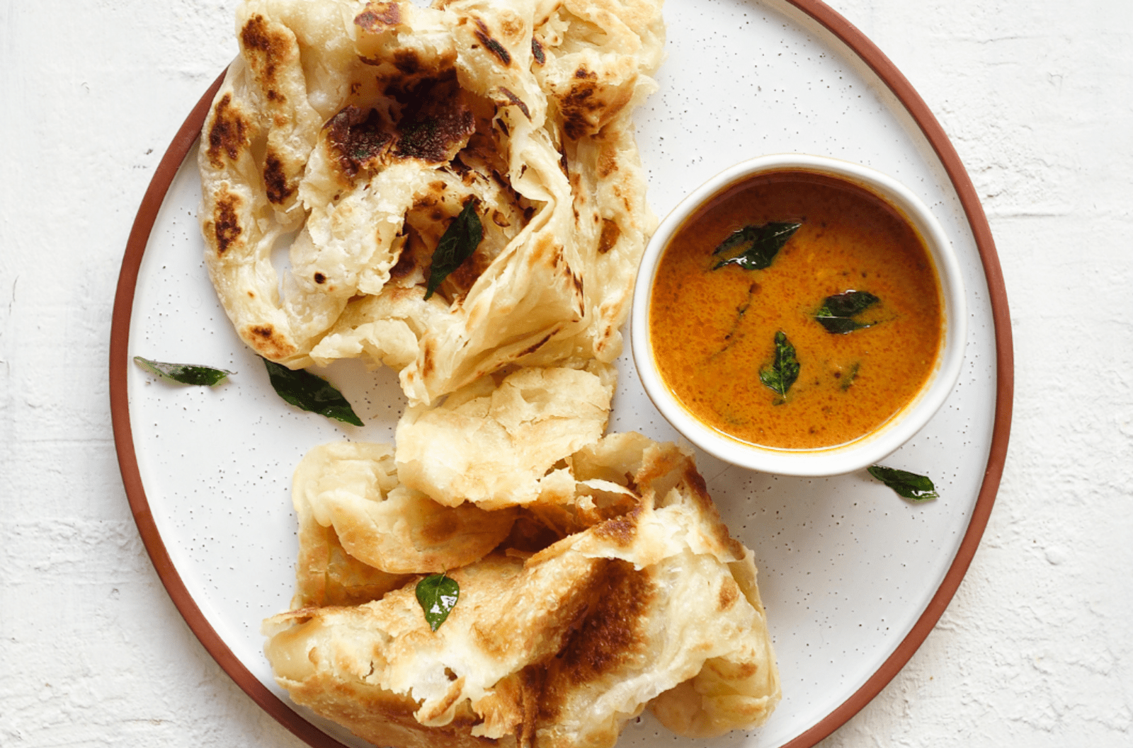 A dish of roti prata served on a white plate with sauce for dipping.