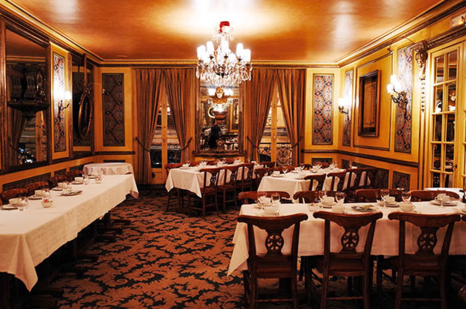Formal dining area with regal wooden chairs, crisp white tablecloths and chandeliers bathing the room in warm light