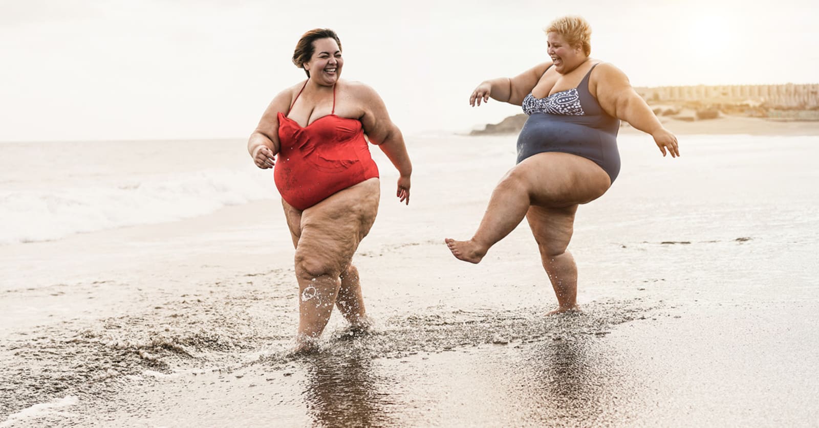 Two women happily walking and splashing through the surf on a bright beach