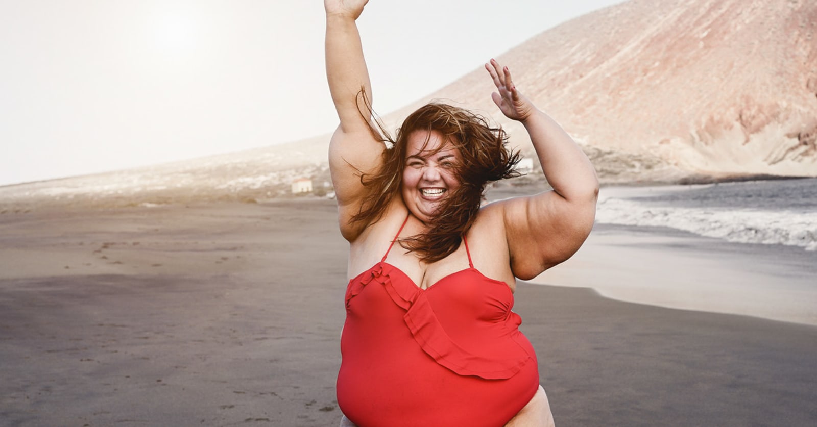 Woman in red swimsuit jumping happily on a grey beach