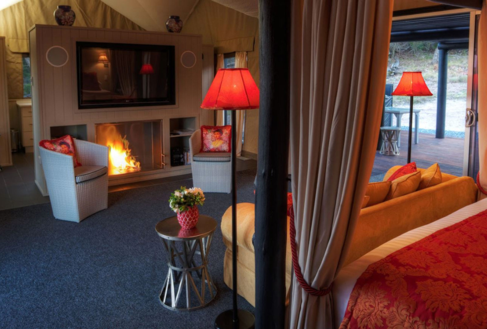 A cozy queen-sized bed, couch, fireplace and entertainment set inside a glamping tent