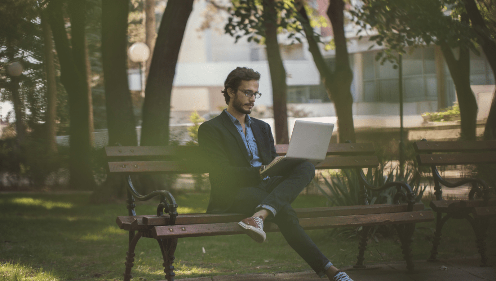 person sits in park on bench with laptop computer