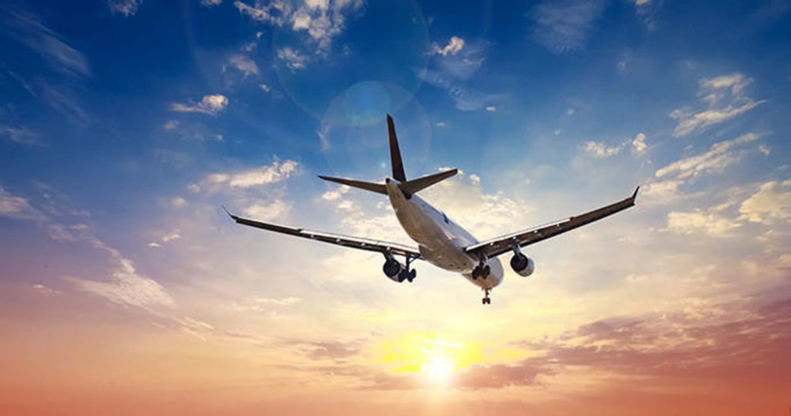 Underside of a plane in the air, with a sunset in the skyline