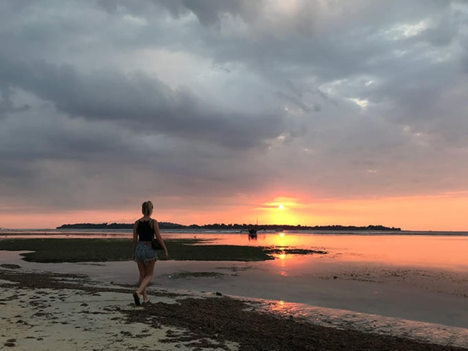 Woman walking towards the water on a beach at sunset.