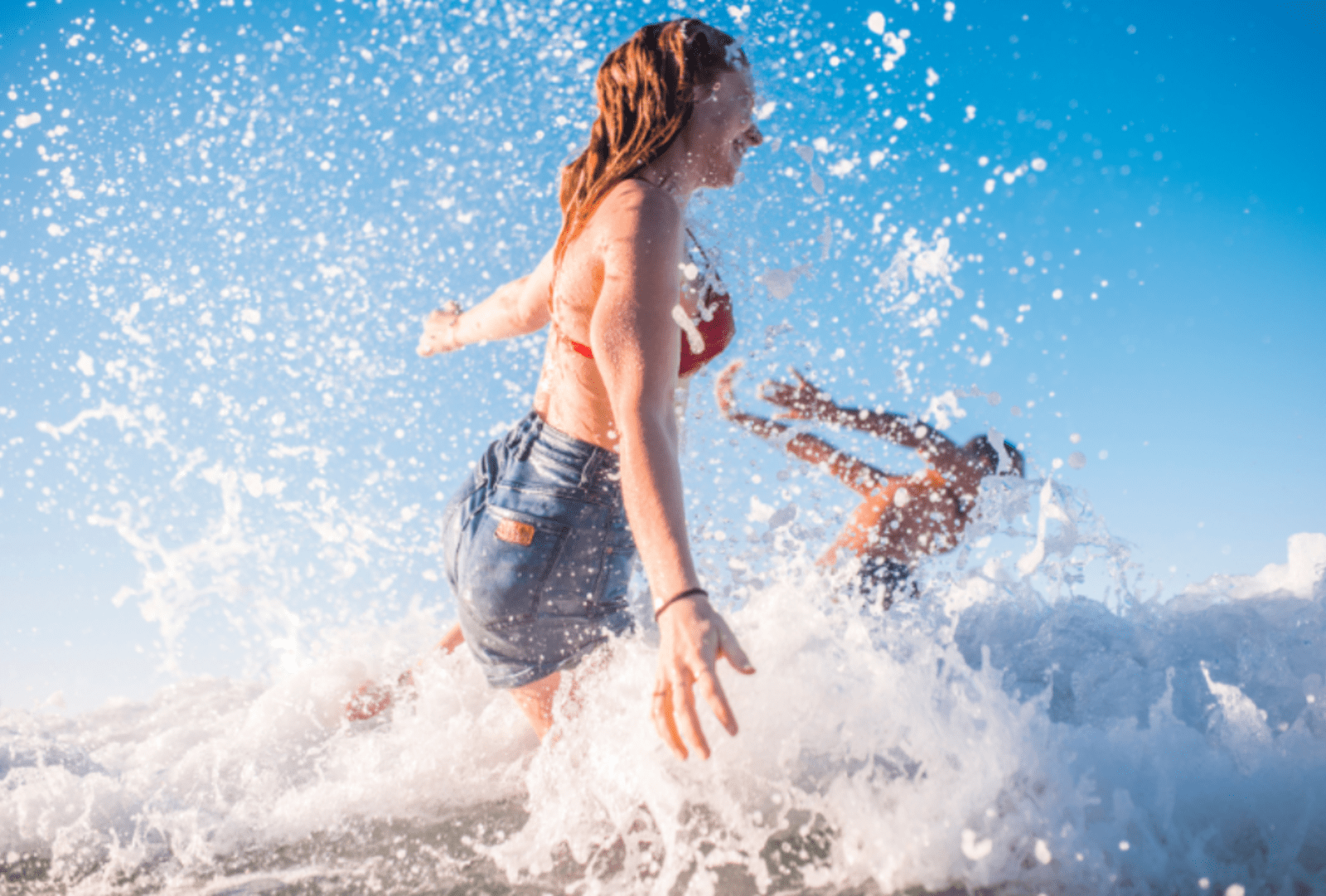 A couple splashing and jumping into the surf.