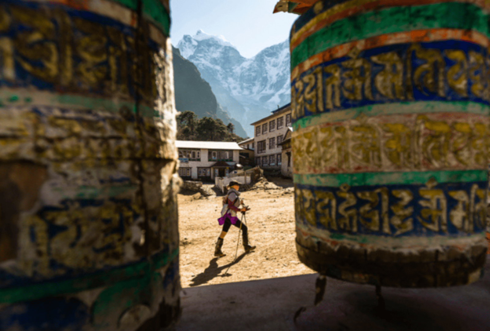 A woman is hiking past prayer wheels at Tengboche Monastery, Nepal